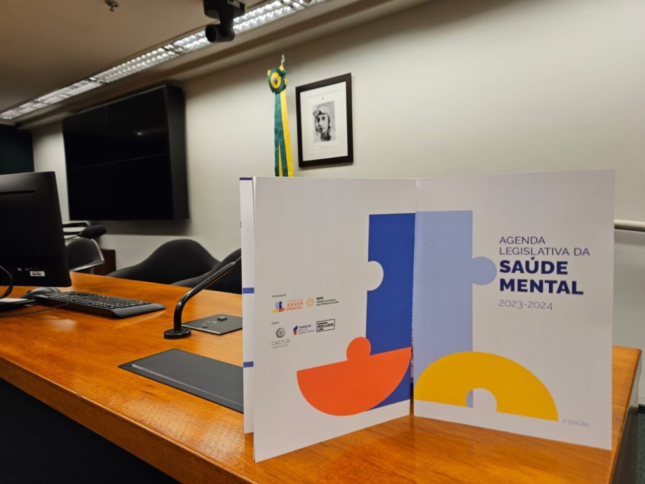 Imagem da capa da Agenda Legislativa da Frente da Saúde Mental de 2023/2024. Documento está sobre uma mesa de uma sala do Congresso Nacional.
